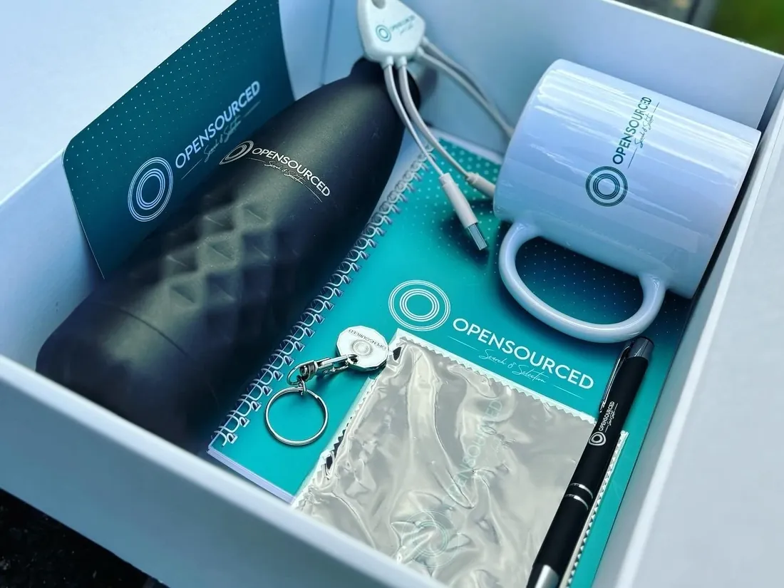 An OpenSourced welcome box with a branded bottle, mug, notebook, pen, keyring and charging cable