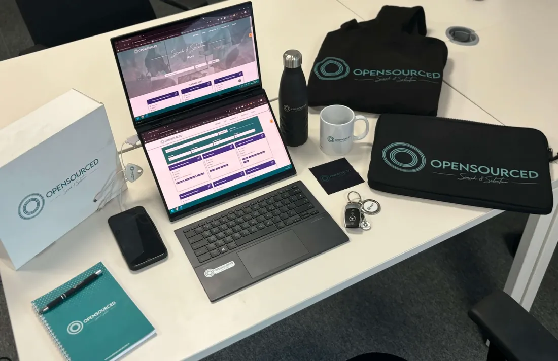 OpenSourced branded hoodie, laptop sleeve, mug, bottle and notebook on a desk